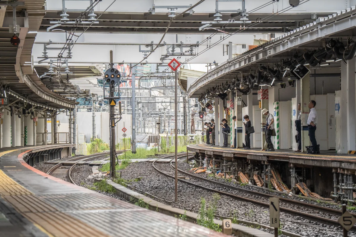 Các sân ga và đường ray tại một nhà ga Tokyo, có hành khách chờ tàu.